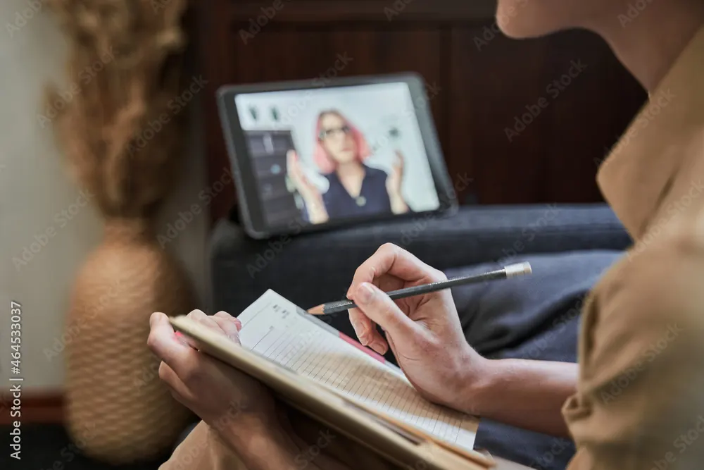 Personne prenant des notes face à une séance en visioconférence